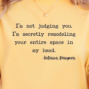 K&ouml;nnte beinhalten: Ein gelbes T-Shirt mit einem humorvollen Zitat &uuml;ber Innenarchitektur: "Ich verurteile dich nicht. Ich renoviere heimlich deinen gesamten Raum in meinem Kopf. -Innenarchitekt"