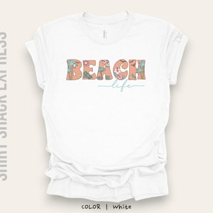 May include: White t-shirt with a floral design that spells out "Beach Life" in a retro font.
