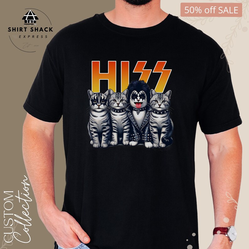 以下が含まれることがあります： KISSのバンドとして扮した4匹の猫のグラフィックが描かれた黒いTシャツ。猫は黒い革のジャケットを着ており、メイクをしており、その上にバンドのロゴ「KISS」があります。