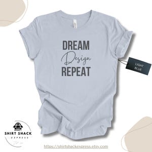 Puede incluir: Camiseta azul claro con las palabras "DREAM Design REPEAT" en letras grises oscuras. Una etiqueta en la camiseta dice "LIGHT BLUE". La camiseta es de Shirt Shack Express.