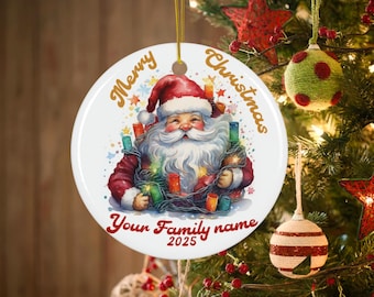 May include: A round Christmas ornament featuring Santa Claus holding lights. The ornament has the words "Merry Christmas" and "Your Family name 2025" in gold and red. The ornament is hanging on a Christmas tree.