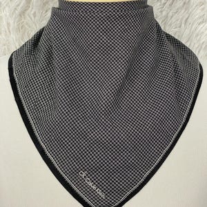 Puede incluir: Un pañuelo a cuadros blancos y negros con borde blanco y el logo "ck Calvin Klein". El pañuelo se muestra sobre una cabeza de maniquí. La tela tiene un pequeño patrón cuadrado.