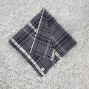 May include: A folded gray and white plaid handkerchief with the Calvin Klein logo. The handkerchief features a classic plaid pattern in shades of gray and white, with a white border.