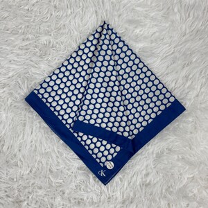 Puede incluir: Un pañuelo azul marino y blanco con lunares. El pañuelo tiene un borde azul oscuro y un estampado de lunares blancos. El logotipo de Calvin Klein es visible en la esquina del pañuelo.