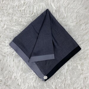 May include: A folded dark gray scarf with a gray border and a black edge. The scarf has a subtle pattern and the Calvin Klein logo is visible. Two small white tags are attached to the scarf.