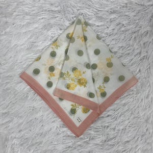 May include: White square scarf with a floral and polka dot pattern. The scarf features yellow flowers and green polka dots. It has a pink border and the Calvin Klein logo is visible.