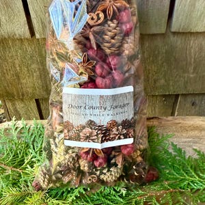 May include: A clear cellophane bag filled with a mix of pine cones, star anise, cinnamon sticks, and red berries. The bag has a label that reads "Door County Forager - Found While Walking". The bag is tied with a natural twine bow.