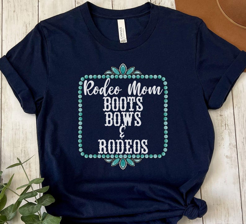 May include: A navy blue t-shirt with a white graphic that says "Rodeo Mom Boots Bows & Rodeos" in a turquoise and white frame.