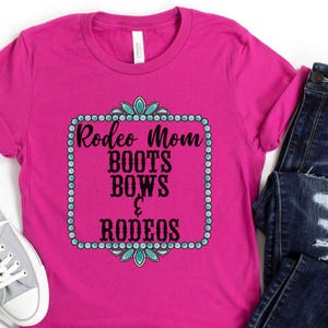 May include: Pink t-shirt with a turquoise and black design that says "Rodeo Mom Boots Bows & Rodeos".