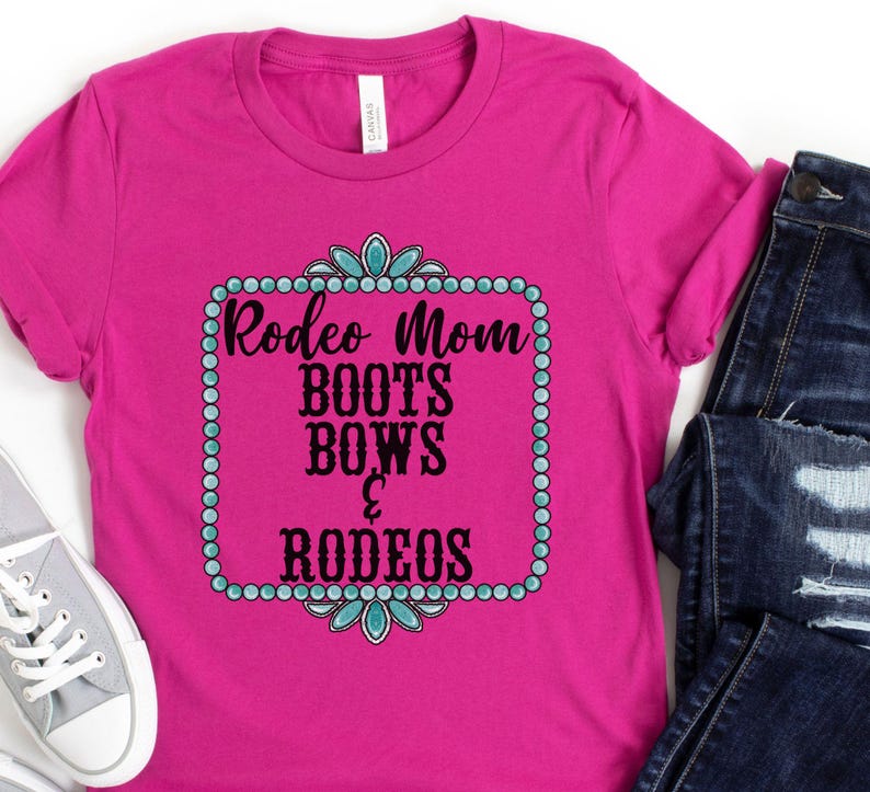 May include: Pink t-shirt with a turquoise and black design that says "Rodeo Mom Boots Bows & Rodeos".