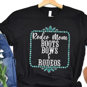 May include: Black t-shirt with a turquoise and white design that says "Rodeo Mom Boots Bows & Rodeos".