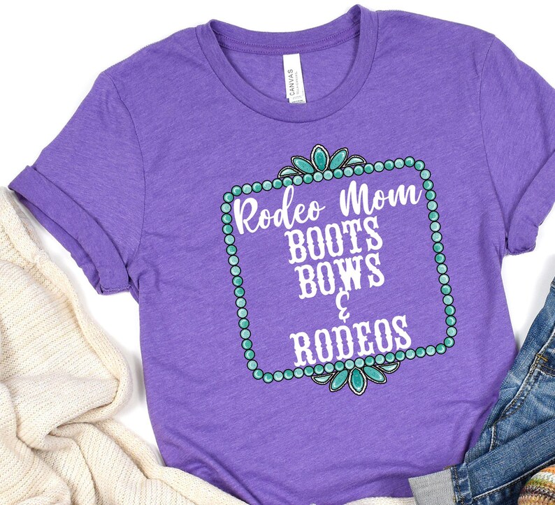 May include: Purple t-shirt with a white graphic that says "Rodeo Mom Boots Bows & Rodeos" in a turquoise and white frame.