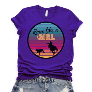 May include: Purple t-shirt with a retro sunset graphic and the text "Rope like a girl".