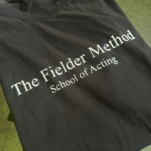 May include: Black t-shirt with white text that reads "The Fielder Method School of Acting."