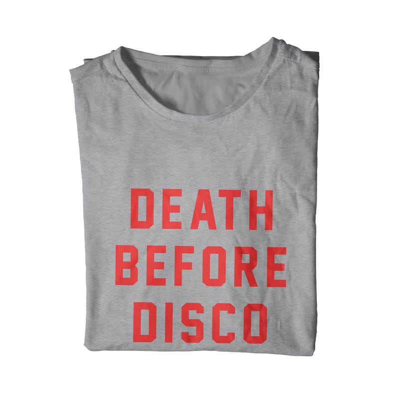 May include: A folded, light gray t-shirt with the words "DEATH BEFORE DISCO" printed in bold, red capital letters. The shirt is made of a soft material and is displayed on a white background.