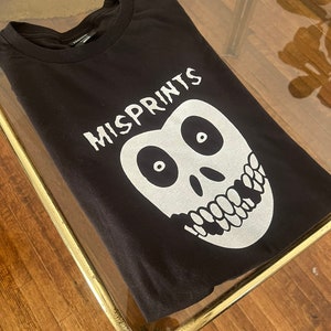 May include: Black t-shirt with a white graphic print of a skull with a toothy grin and the word "MISPRINTS" above it.