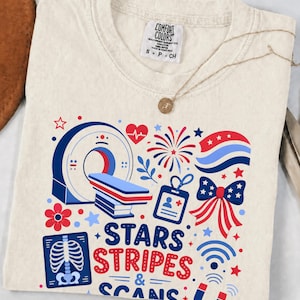 Könnte beinhalten: Ein cremefarbenes T-Shirt mit einem Grafikdruck, der einen CT-Scanner, ein Röntgenbild eines Brustkorbs, einen medizinischen Ausweis, eine Schleife, Feuerwerk und den Text "STARS STRIPES & SCANS" in Rot und Blau zeigt. Mit Comfort Colors Etikett.