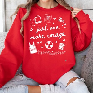 May include: A red crew neck sweatshirt featuring the text "just one more image" in white, along with medical-themed illustrations. The design includes an X-ray, radiation symbol, and an apron. The sweatshirt is a vibrant red colour.