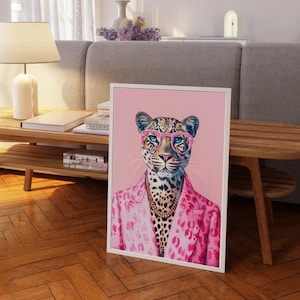 Puede incluir: Una impresión enmarcada en rosa y blanco de un leopardo con gafas rosas y una chaqueta rosa de estampado de leopardo. El fondo es de color rosa claro.