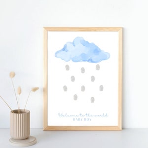 以下が含まれることがあります： 水彩画の薄い青色の雲と指紋の雨滴が描かれたフレーム入りのプリント。テキスト「Welcome to the world BABY BOY」は繊細な青色のスクリプトで書かれています。フレームは明るい色の木材で作られています。