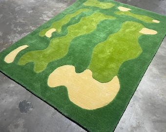 May include: A rectangular area rug featuring a tufted surface with an abstract pattern of organic, flowing shapes in varying shades of forest green, lime green, and pale yellow, creating a layered, multi-dimensional visual effect.