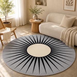 May include: A circular rug featuring a light grey backdrop with a black sunburst pattern emanating from a cream-coloured central circle. The rug is positioned on a light-toned floor within a living room.