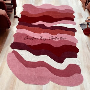 May include: A pink, red, and white abstract area rug with a wavy design. The rug has a "Creative Rugs Collection" label in the center.