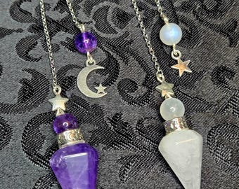 May include: Two crystal pendulums with silver chains. One features a purple amethyst crystal and a crescent moon charm, the other a clear quartz crystal and a star charm. Both have a star at the top.