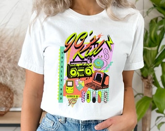 May include: White t-shirt with a graphic print of a 90s kid theme. The graphic includes a boombox, a game console, a computer, and other 90s icons. The text on the graphic says "90's Kid" and "Totally Rad Summer of '95".