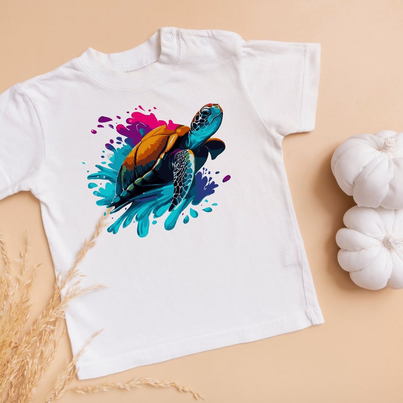 K&ouml;nnte beinhalten: Wei&szlig;es T-Shirt mit einem bunten Grafikdruck einer Meeresschildkr&ouml;te, die in einem Spritzer blauen, violetten und rosafarbenen Wassers schwimmt.