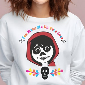 May include: White sweatshirt with a colorful graphic of a character from the movie Coco. The text "You Make Me Un Poco Loco" is written in a colorful font around the character.