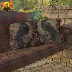 May include: Two throw pillows with a brown and green floral pattern and black crows perched on branches. The pillows are on a brown plaid swing bench.