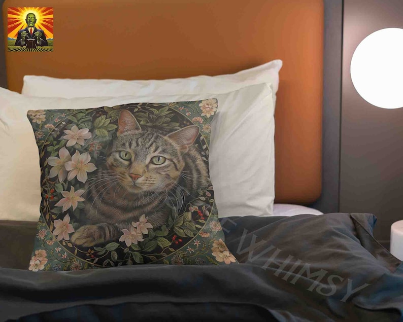 May include: A square throw pillow featuring a detailed illustration of a brown tabby cat centered within a circular frame of green leaves, small red berries, and pale pink flowers against a dark background. The cat has green eyes and whiskers.