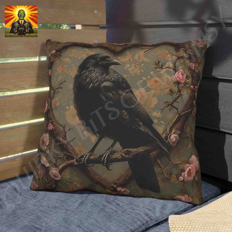 May include: A decorative throw pillow with a black crow perched on a branch with pink flowers. The crow is in a heart-shaped frame with a floral background.