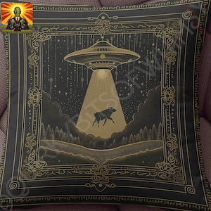 May include: Black square pillow with a gold-colored illustration of a UFO beaming a cow. The design is set against a dark background with a starry sky and a forest. The pillow has a decorative gold border.
