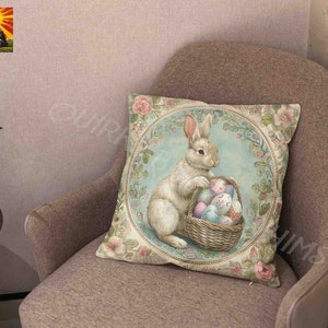May include: A white bunny with pink ears sits in a wicker basket filled with colorful Easter eggs. The bunny is surrounded by floral designs and a blue background. The image is on a throw pillow.