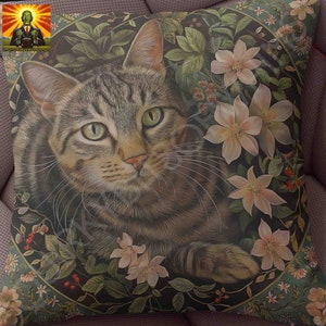 May include: A square throw pillow featuring a detailed illustration of a brown tabby cat with green eyes. The cat is centered within a circular frame surrounded by light pink flowers, green leaves, and small red berries against a dark background.