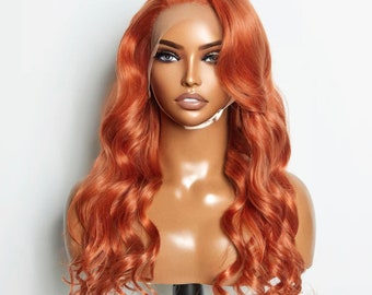 May include: A long, wavy, copper-colored human hair wig on a mannequin head. The wig has a lace front and is styled in loose waves.