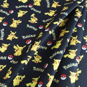 May include: Black fabric with a repeating pattern of yellow Pikachu characters and the word "Pokémon" in blue. The fabric is folded over itself, showing the pattern on both sides.