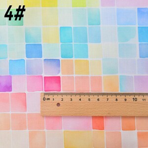 May include: A close-up of a fabric with a watercolor design of colorful squares. The fabric is white with a grid of squares in shades of blue, pink, yellow, and orange. A ruler is placed on the fabric, showing the scale in centimeters.