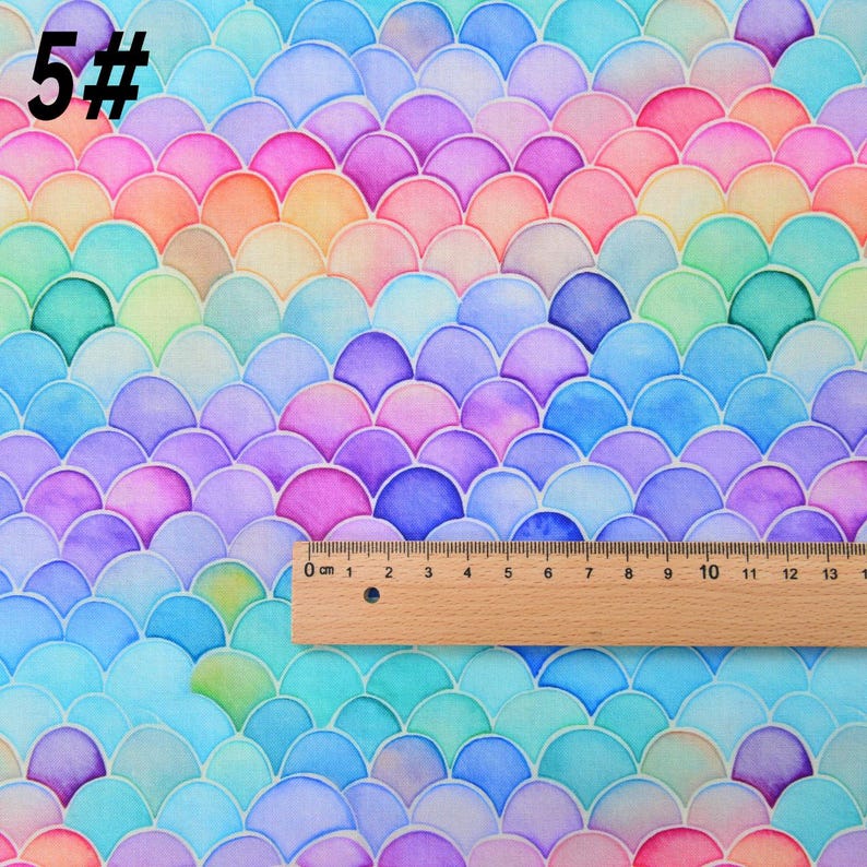 May include: A colorful fabric with a mermaid scale pattern in shades of blue, green, purple, pink, and orange. The fabric is measured with a ruler in inches.
