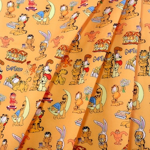 May include: Orange fabric with a repeating pattern of Garfield the cat and other characters. The design includes Garfield on a skateboard, holding flowers, and with a sandwich. The word "Garfield" is also printed on the fabric.