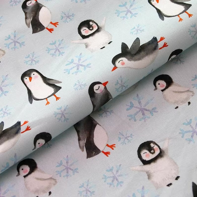 Pode incluir: Um tecido azul com um padr&atilde;o repetitivo de pinguins e flocos de neve. Os pinguins est&atilde;o em v&aacute;rias poses, alguns est&atilde;o em p&eacute;, alguns est&atilde;o nadando e alguns est&atilde;o voando. Os flocos de neve s&atilde;o brancos e t&ecirc;m um efeito aquarela.