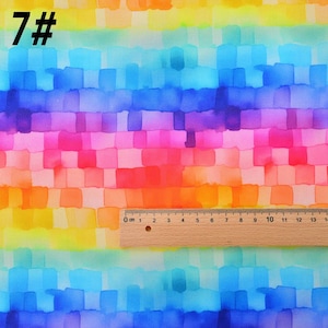 May include: A colorful fabric with a watercolor-like design of squares in shades of blue, purple, pink, orange, and yellow. The fabric has a ruler measuring 13 inches in length.