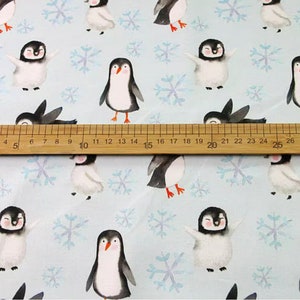 Pode incluir: Um tecido azul claro com um padr&atilde;o repetitivo de pinguins e flocos de neve. Os pinguins est&atilde;o em v&aacute;rias poses, alguns est&atilde;o em p&eacute;, alguns est&atilde;o caminhando e alguns est&atilde;o estendendo suas asas. Os flocos de neve s&atilde;o de cor azul claro e est&atilde;o dispersos por todo o tecido.