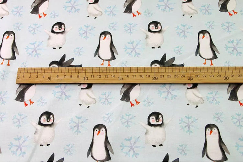Pode incluir: Um tecido azul claro com um padr&atilde;o repetitivo de pinguins e flocos de neve. Os pinguins est&atilde;o em v&aacute;rias poses, alguns est&atilde;o em p&eacute;, alguns est&atilde;o caminhando e alguns est&atilde;o estendendo suas asas. Os flocos de neve s&atilde;o de cor azul claro e est&atilde;o dispersos por todo o tecido.