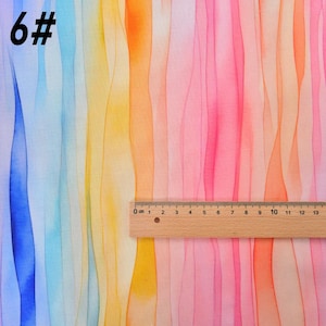 May include: A colorful fabric with vertical stripes of blue, yellow, orange, pink, and red. The fabric has a watercolor effect, with the colors blending together. A ruler is placed on the fabric, showing the measurement in centimeters.