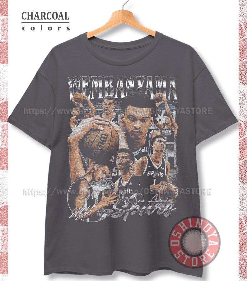 May include: A charcoal gray t-shirt featuring a vintage-style graphic print of basketball player Victor Wembanyama in various poses, including holding a basketball. The text WEMBANYAMA and San Antonio Spurs is printed in a distressed white font.