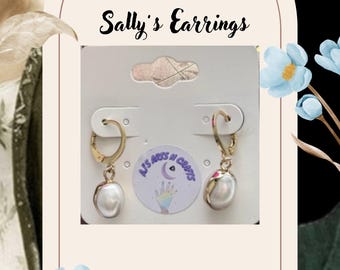 May include: Gold-coloured hoop earrings with a dangling, pear-shaped white pearl. The earrings are displayed on a white card with the text "Sally's Earrings". The background features floral accents and a woman's image.