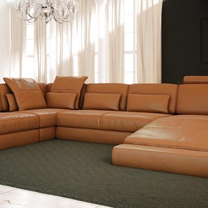 May include: A large, tan leather sectional sofa with a chaise lounge. The sofa has multiple cushions and a modern design.